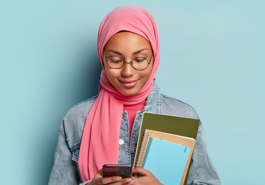One of Qwell's counsellor's, a muslim woman wearing a peach hijab and holding a caseload of files, smiling as she looks slightly off camera.
